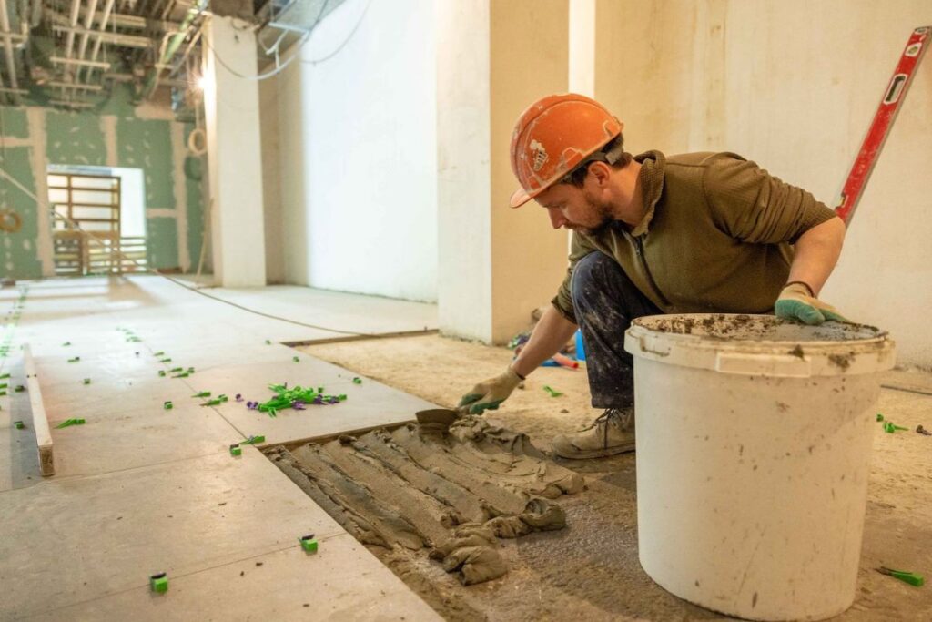 A professional tile setter on a construction site carefully installing ceramic floor tiles.