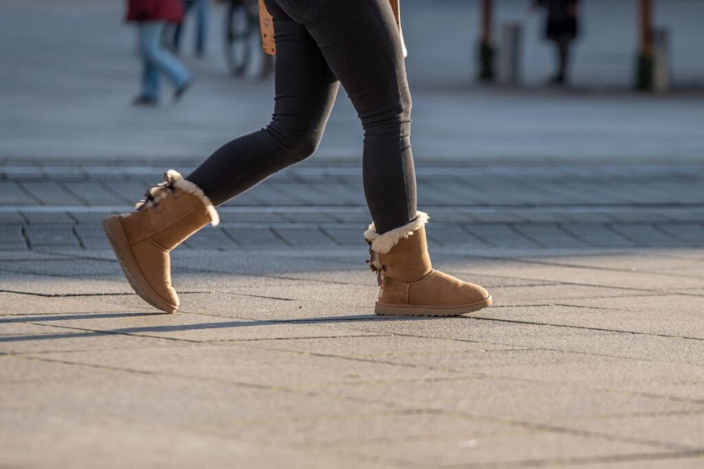 A trendy woman walks in UGG Mini Bailey Bow II Boots in a chestnut color